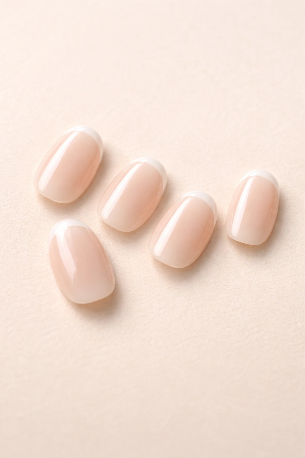 Close-up of five micro-French short oval press-on nails on a neutral surface