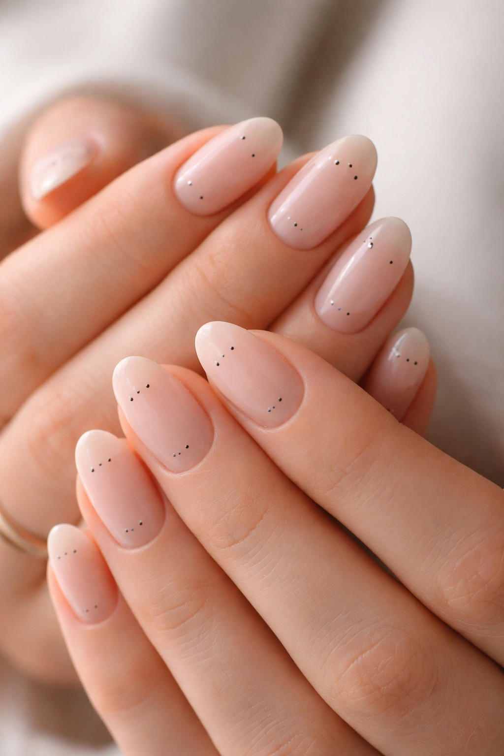 Close-up of hands with short almond nails featuring tiny dot patterns near base and tips