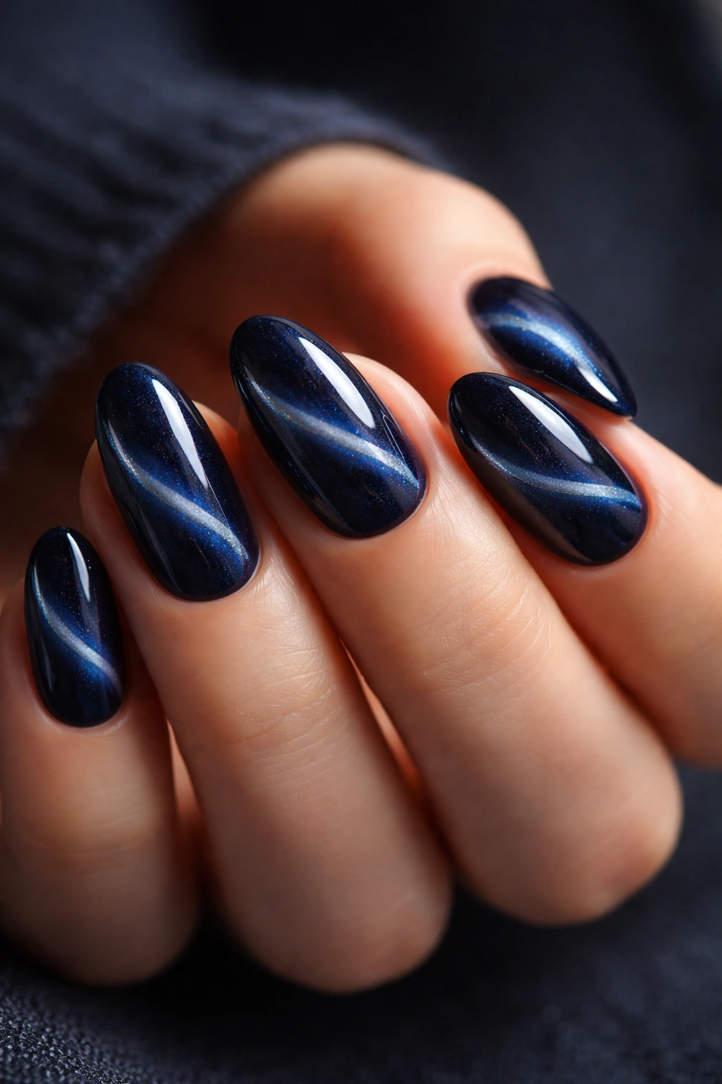Close-up of short almond nails in midnight blue with cat-eye shimmer