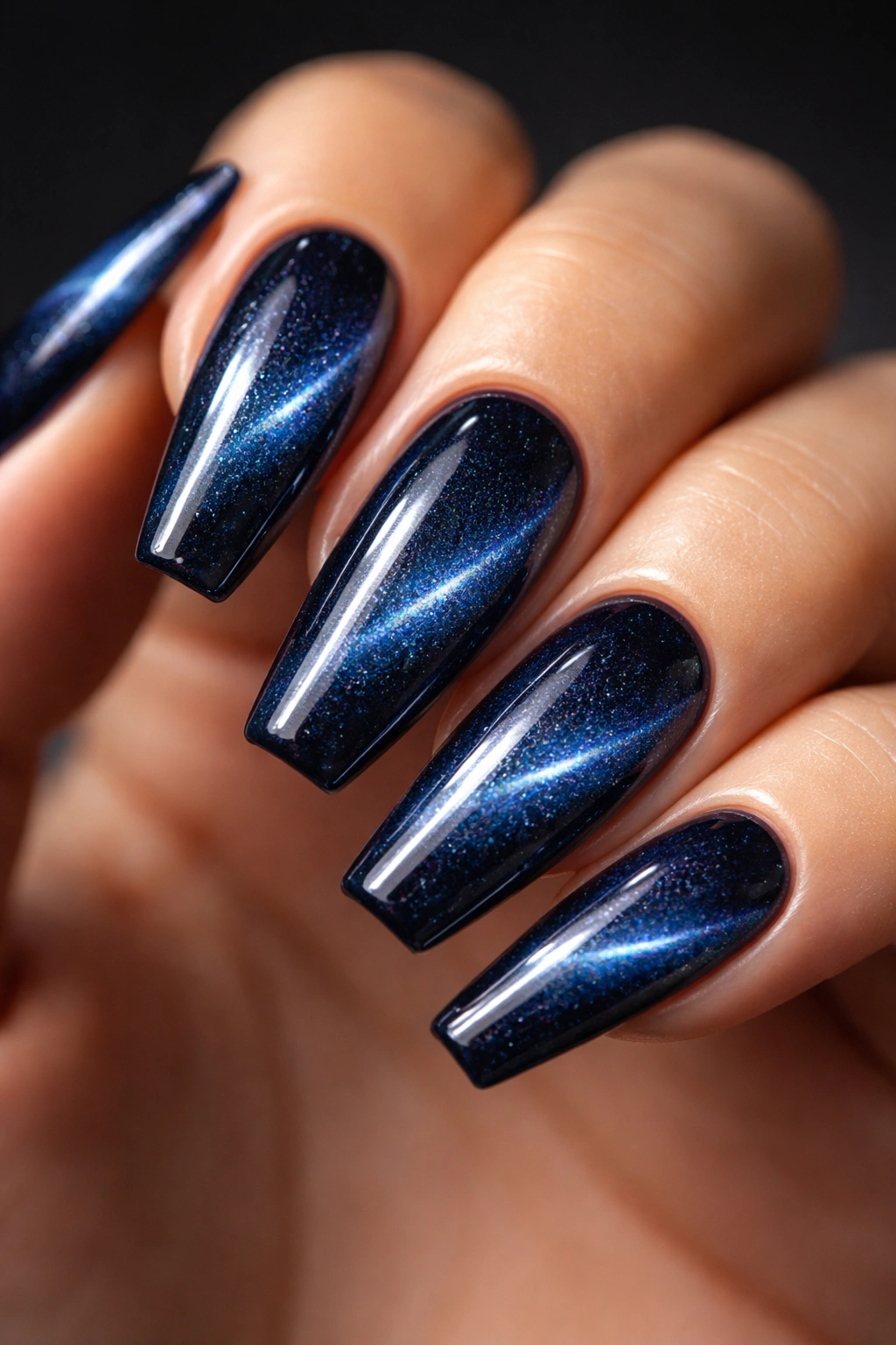 Midnight blue cat eye nails with a side-swept beam on a dark background