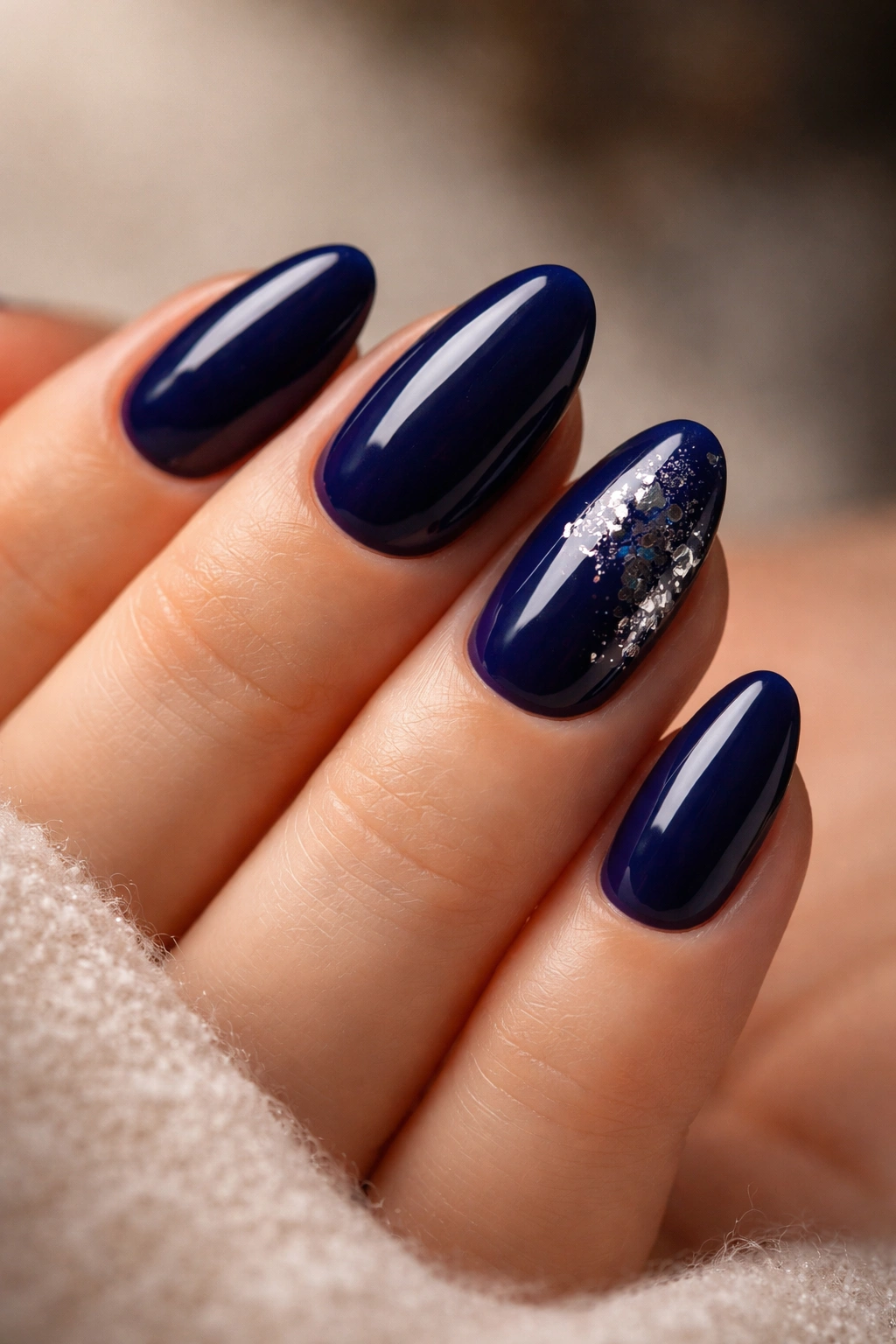 Close-up of short almond nails in glossy midnight blue with a single accent nail