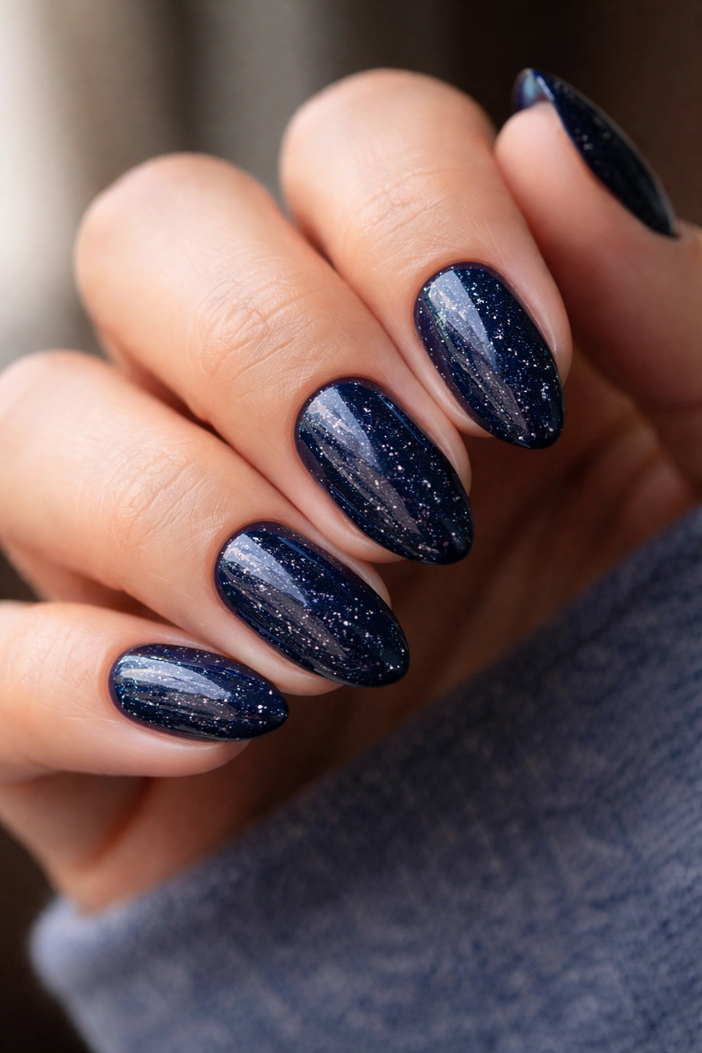 Close-up of midnight blue almond nails with fine silver flecks and glossy finish.