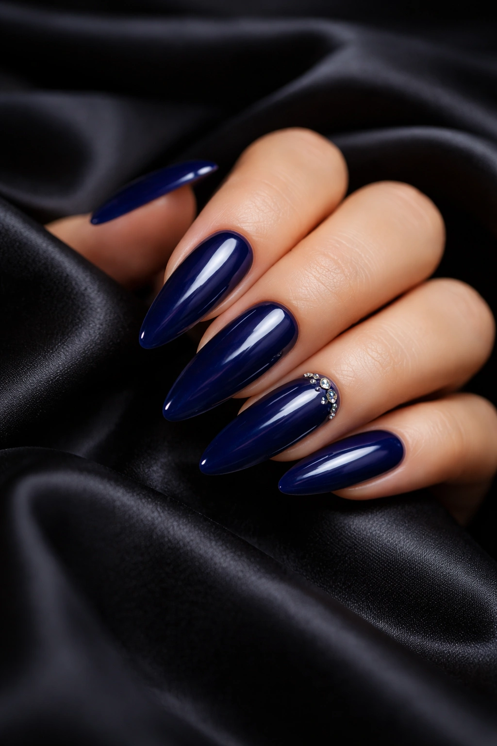 Deep midnight blue oval nails with small rhinestones near cuticle