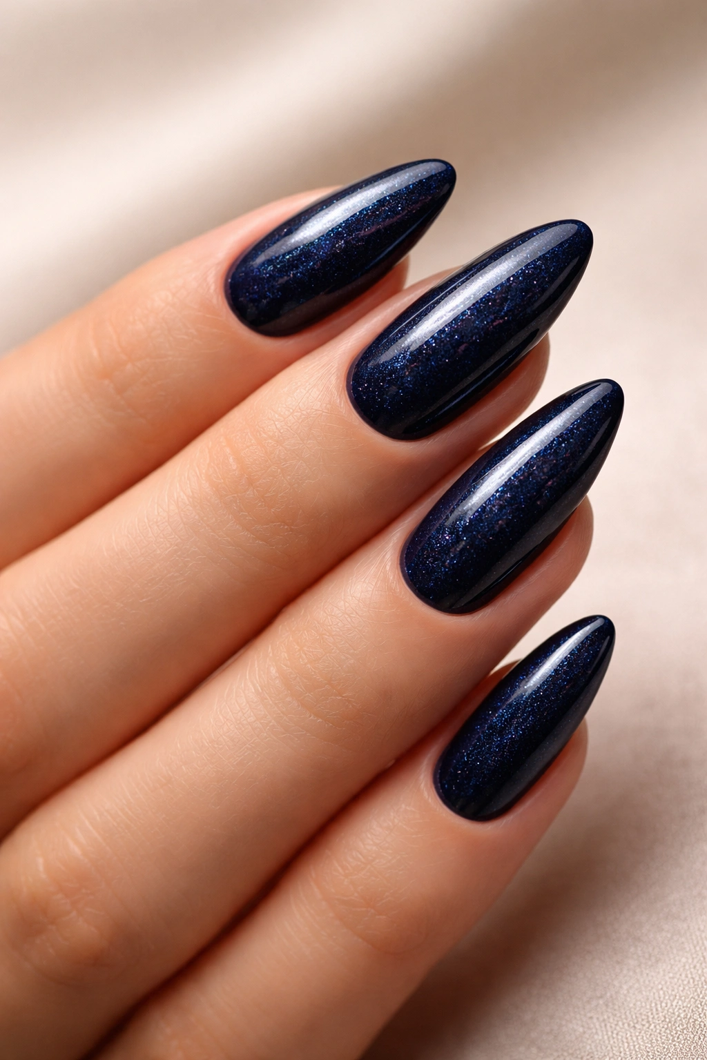Close-up of midnight blue almond nails with subtle sparkle under soft lighting.