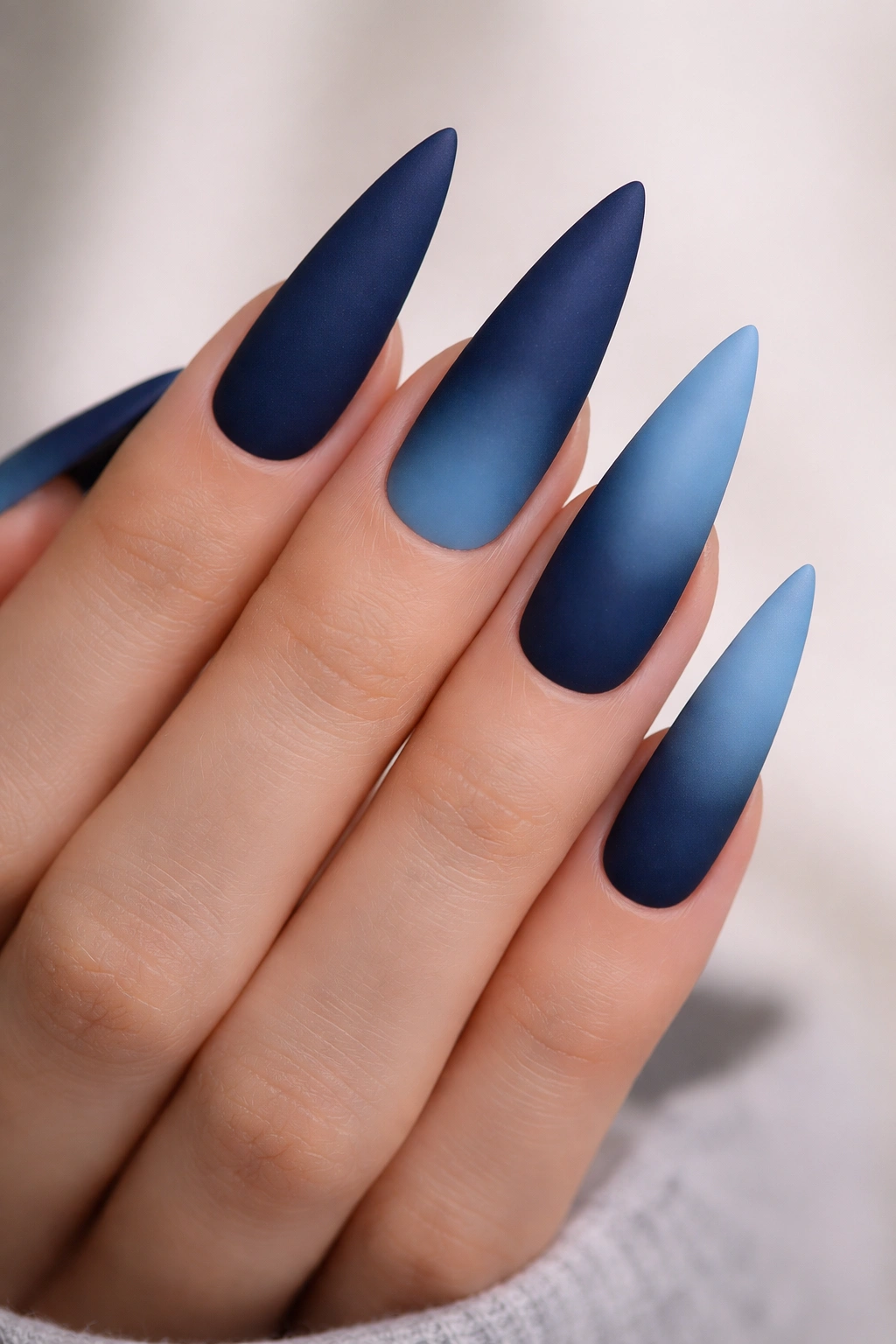Close-up of stiletto nails with midnight to sky blue matte ombre