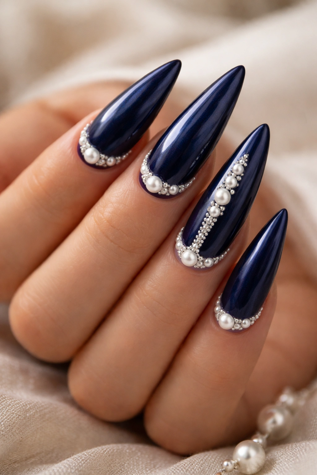 Midnight blue stiletto nails with pearl accents on a neutral backdrop.