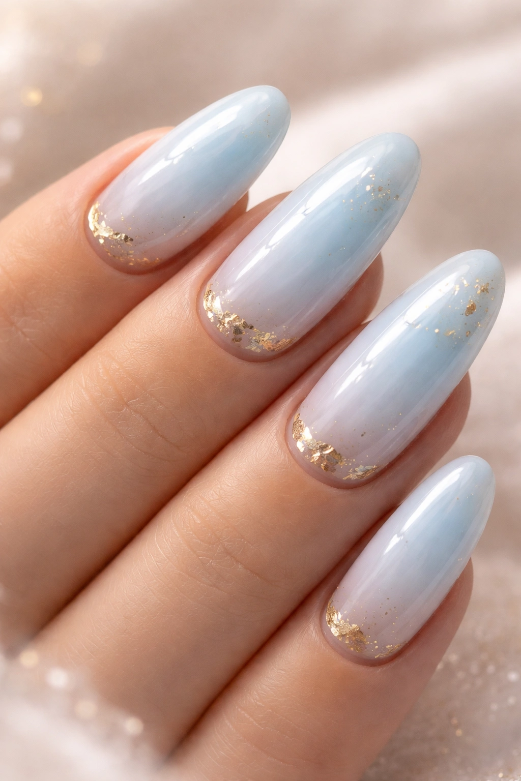 Close-up of long oval nails in pale blue milk bath with gold accents