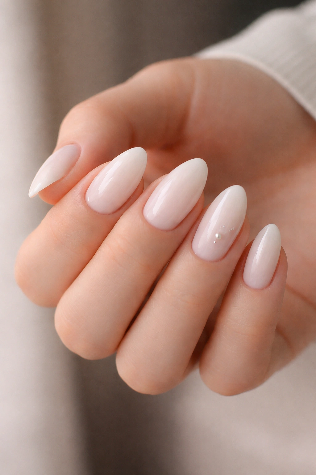 Close-up of milky white almond nails with a single accent nail featuring a tiny pearl