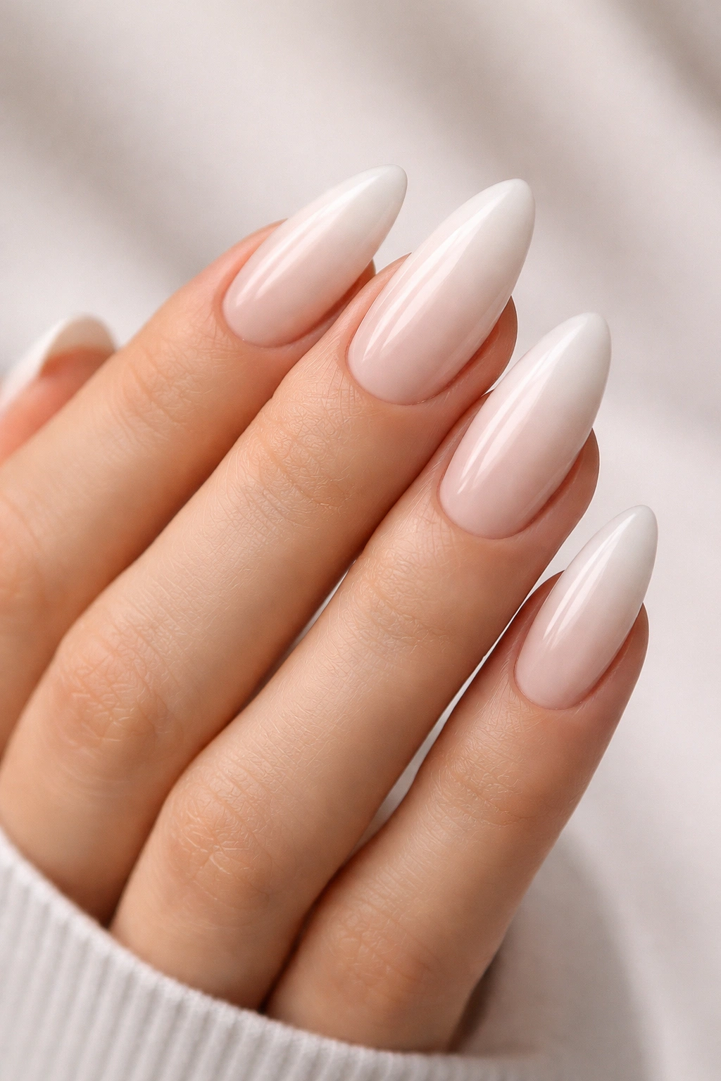 Close-up of milky white almond nails with nude cuticle shadow on a bare hand