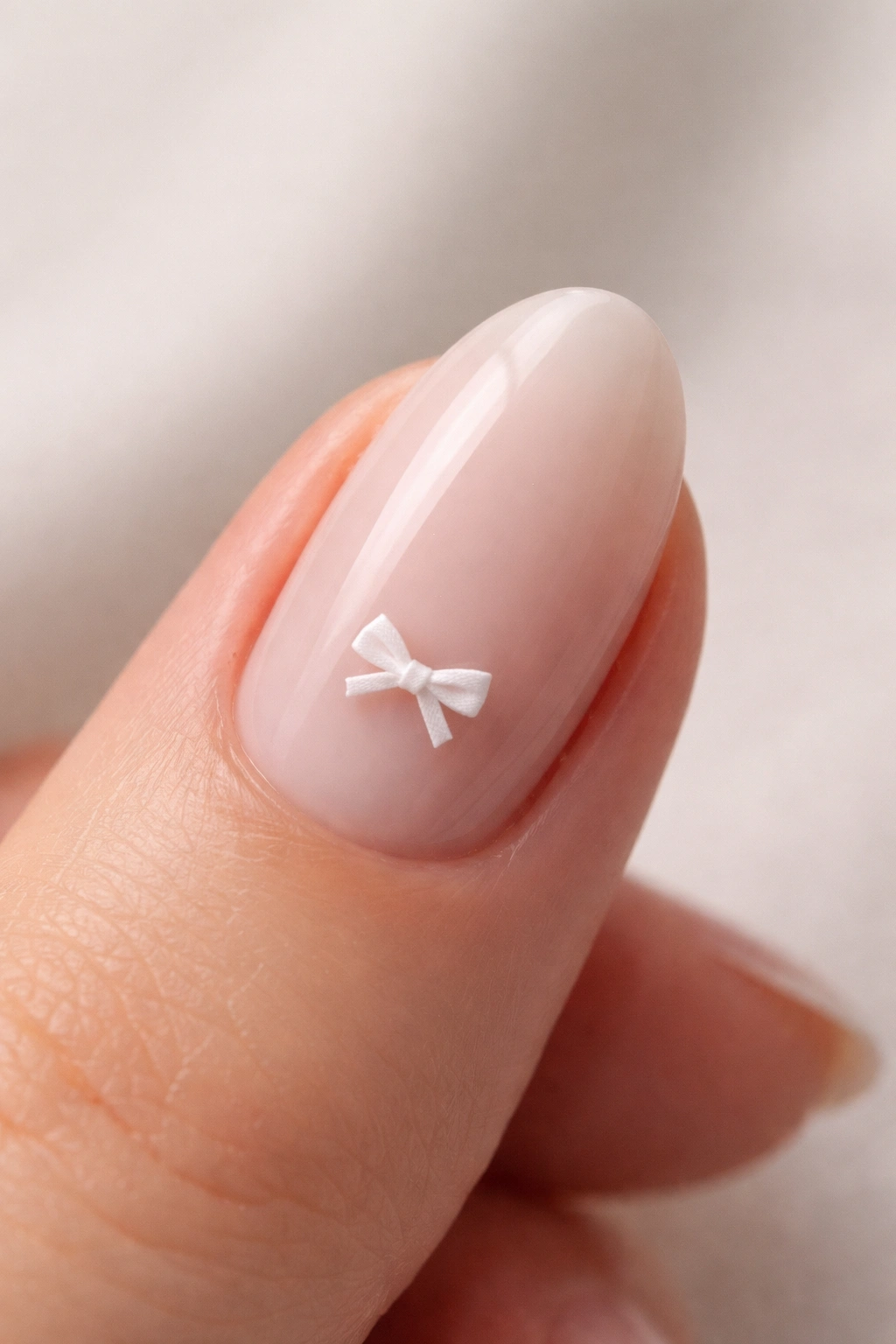 Close-up of a short almond nail with milky base and tiny white bow, glossy finish