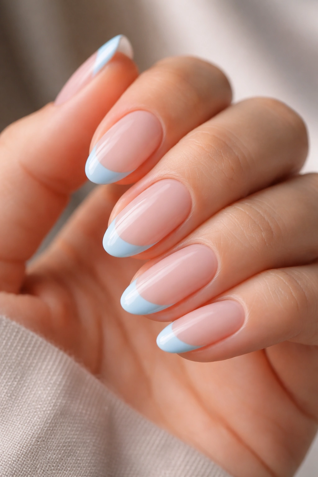 Close-up of short almond nails with milky pink base and blue French tips