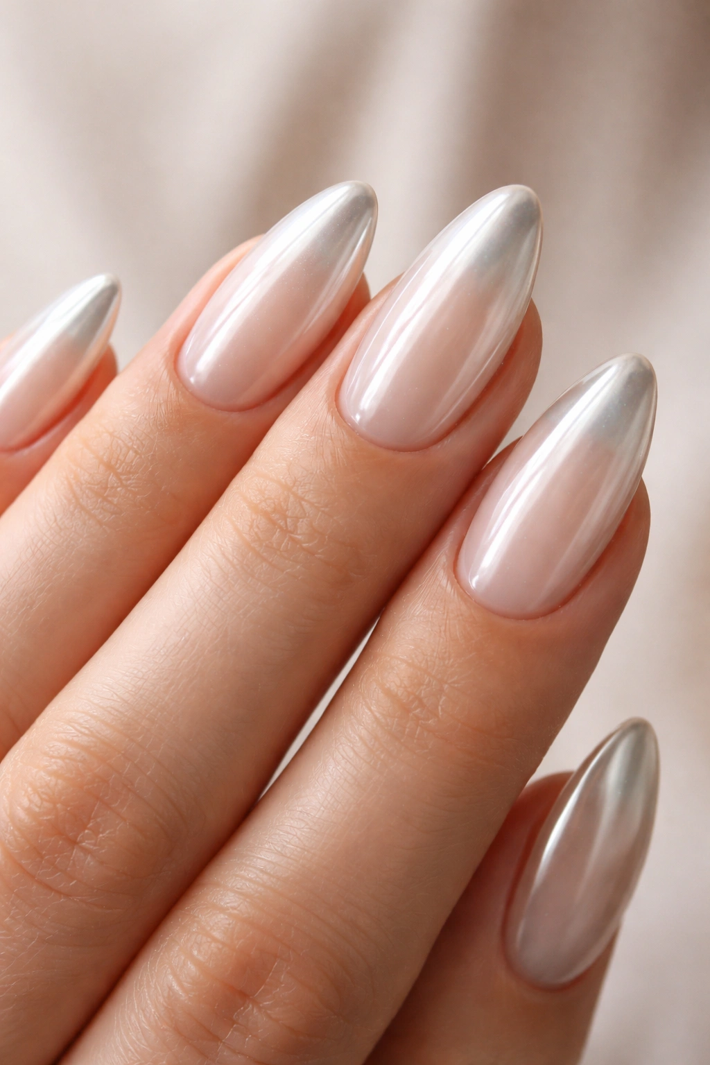 Close-up of almond-shaped nails with milky white base and chrome tips.