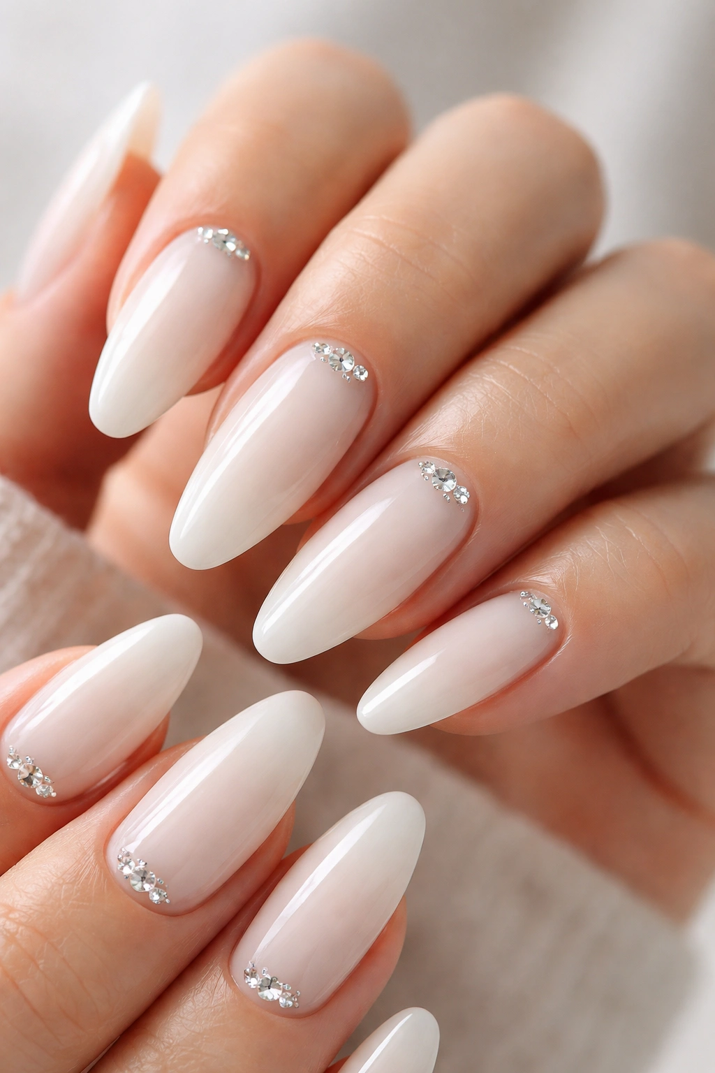 Close-up of milky white almond nails with crystal accents on a bare hand