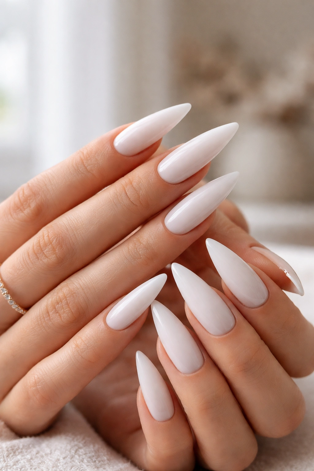 Close-up of milky white stiletto nails in a minimalist studio setting