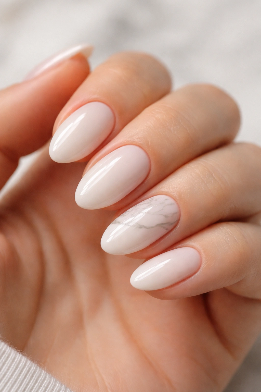 Close-up of short almond milky nails with soft white marble veining on one accent nail