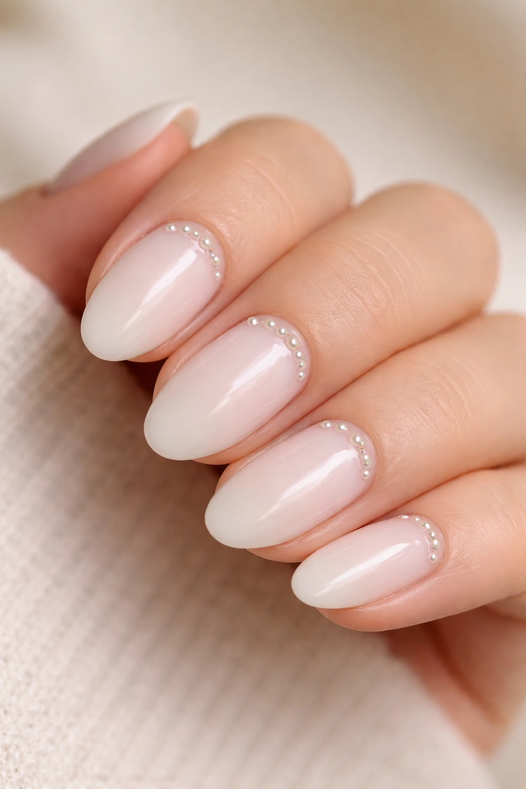 Close-up of short almond nails with milky base and micro pearls near cuticle