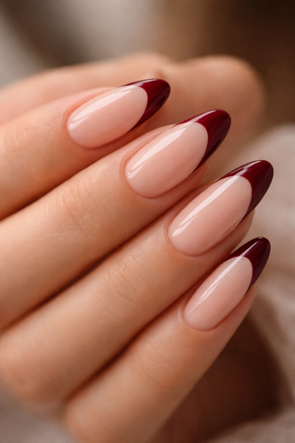 Close-up of almond nails with milky nude base and deep red French tips