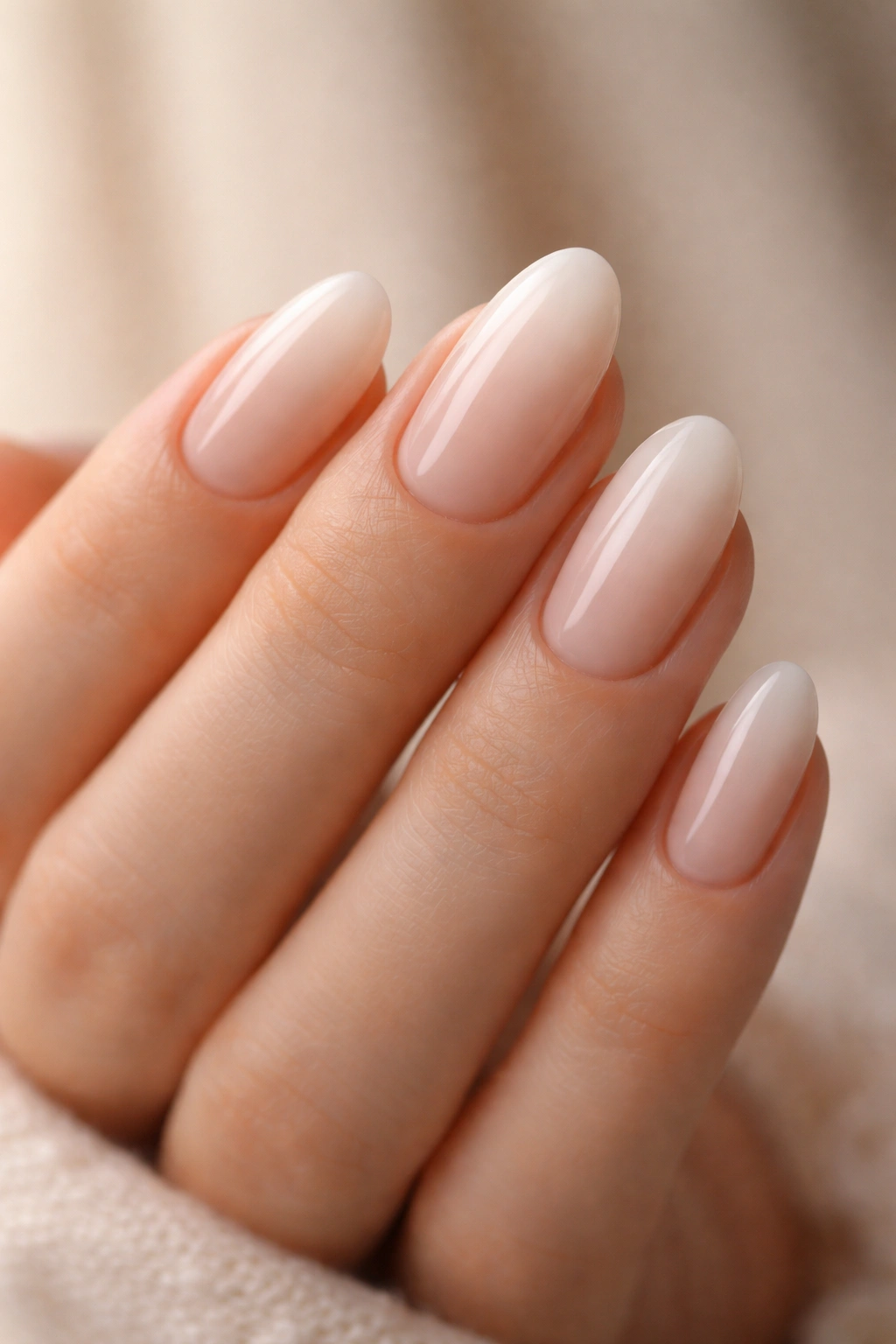 Close-up of short almond nails with milky nude fade and glossy finish