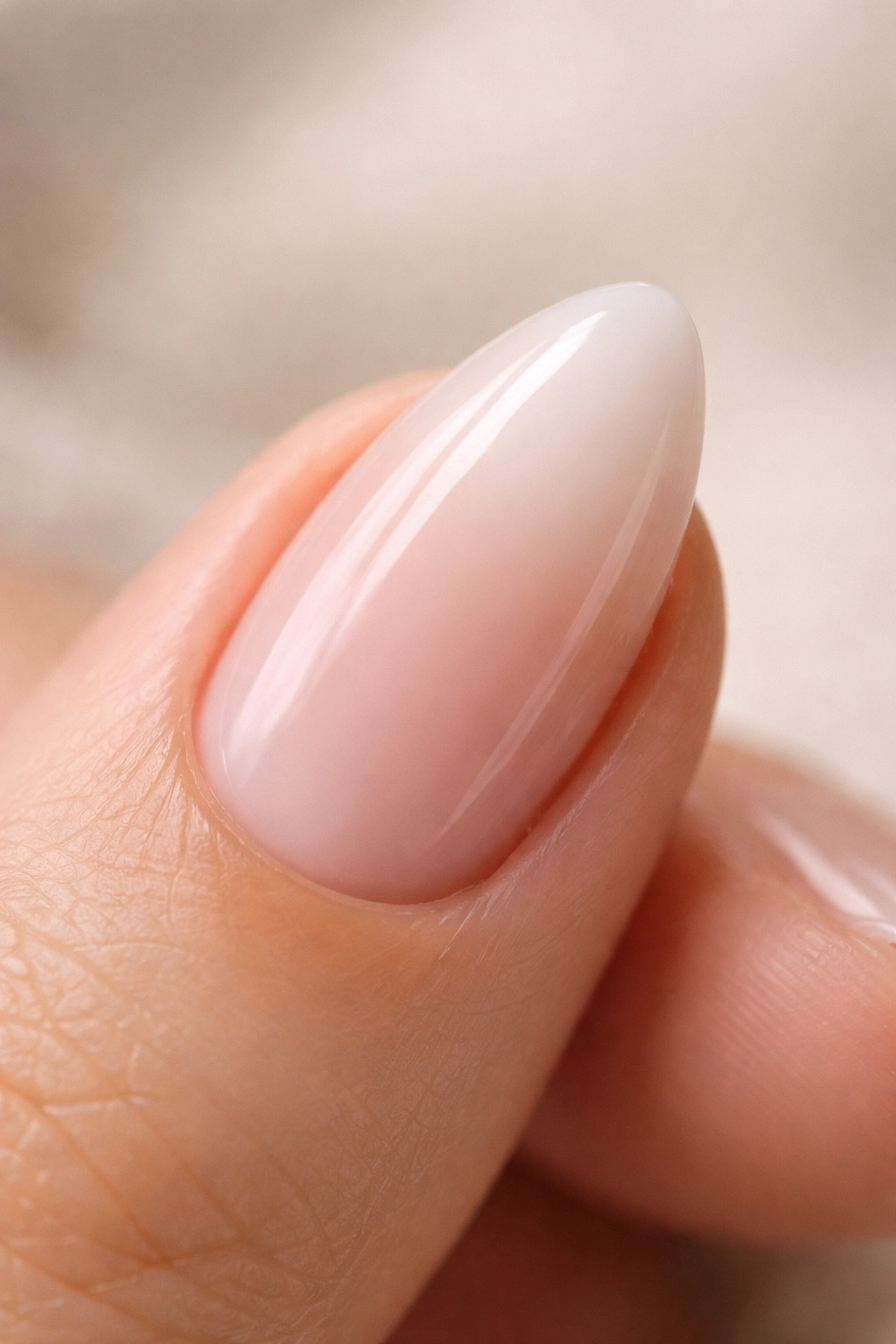 Close-up of a short almond nail with a milky translucent nude finish.