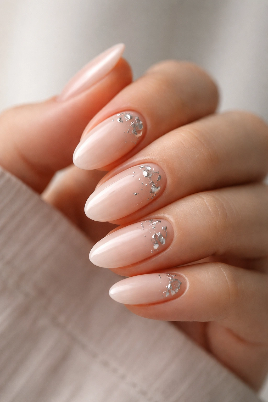 Close-up of milky nude almond nails with scattered silver foil
