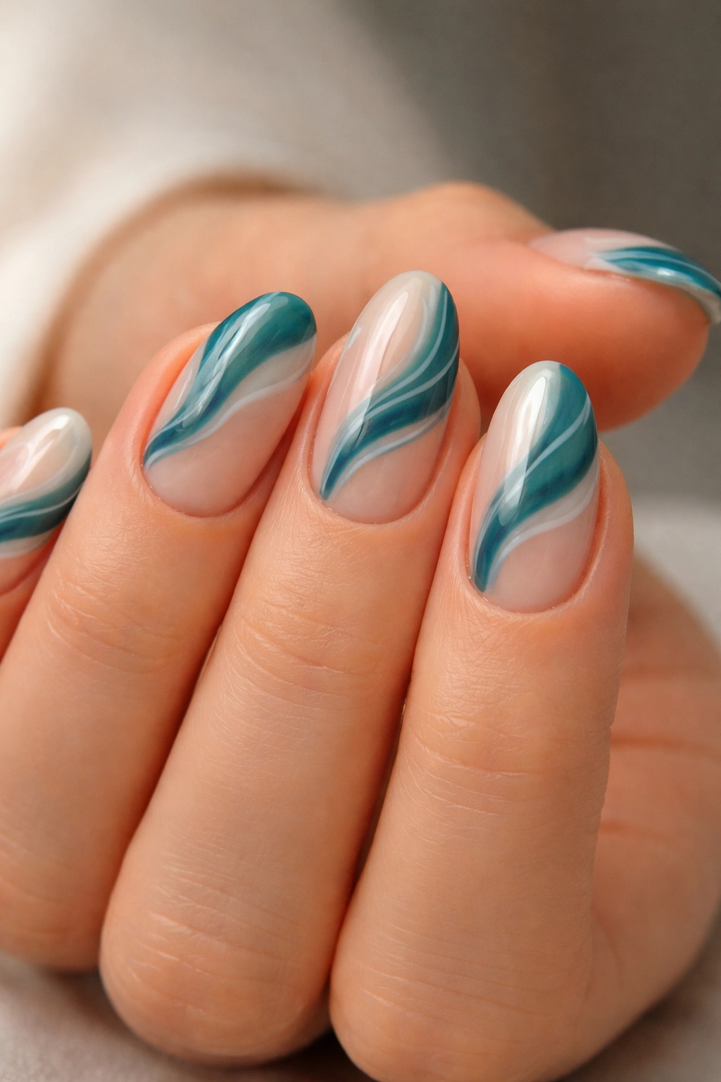 Close-up of milky nude nails with teal abstract waves on short almond nails