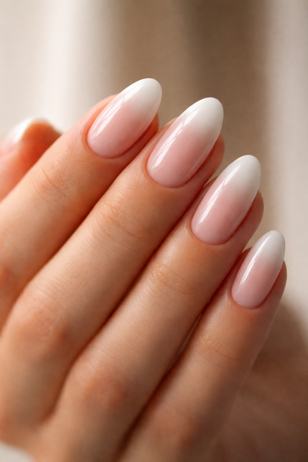 Close-up of short almond nails with pink-nude base fading to milky white tips