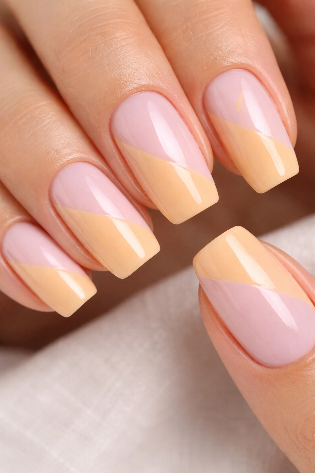 Nails with milky pink and apricot diagonal color blocks on a hand