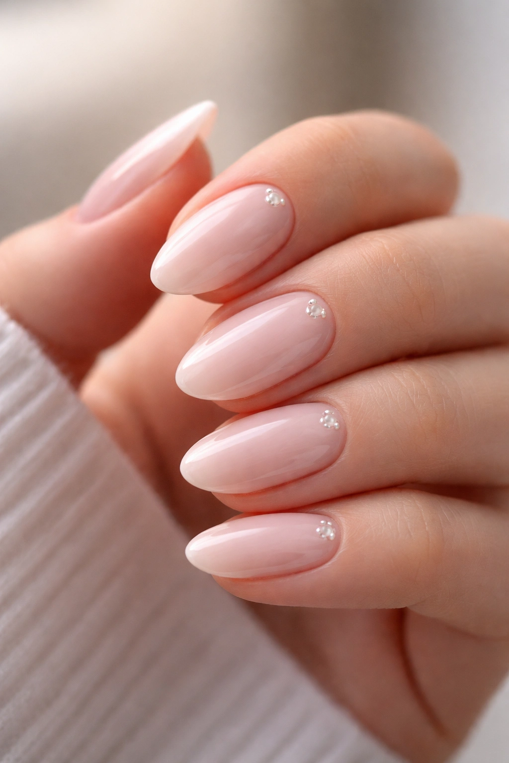 Close-up of short milky pink almond nails with tiny pearl accents on a hand