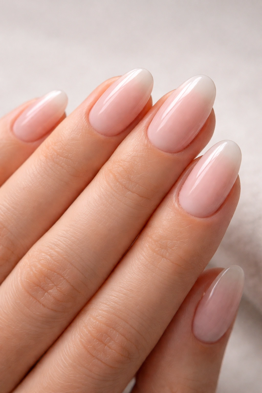 Close-up of short almond nails with milky pink ombre and barely-there finish