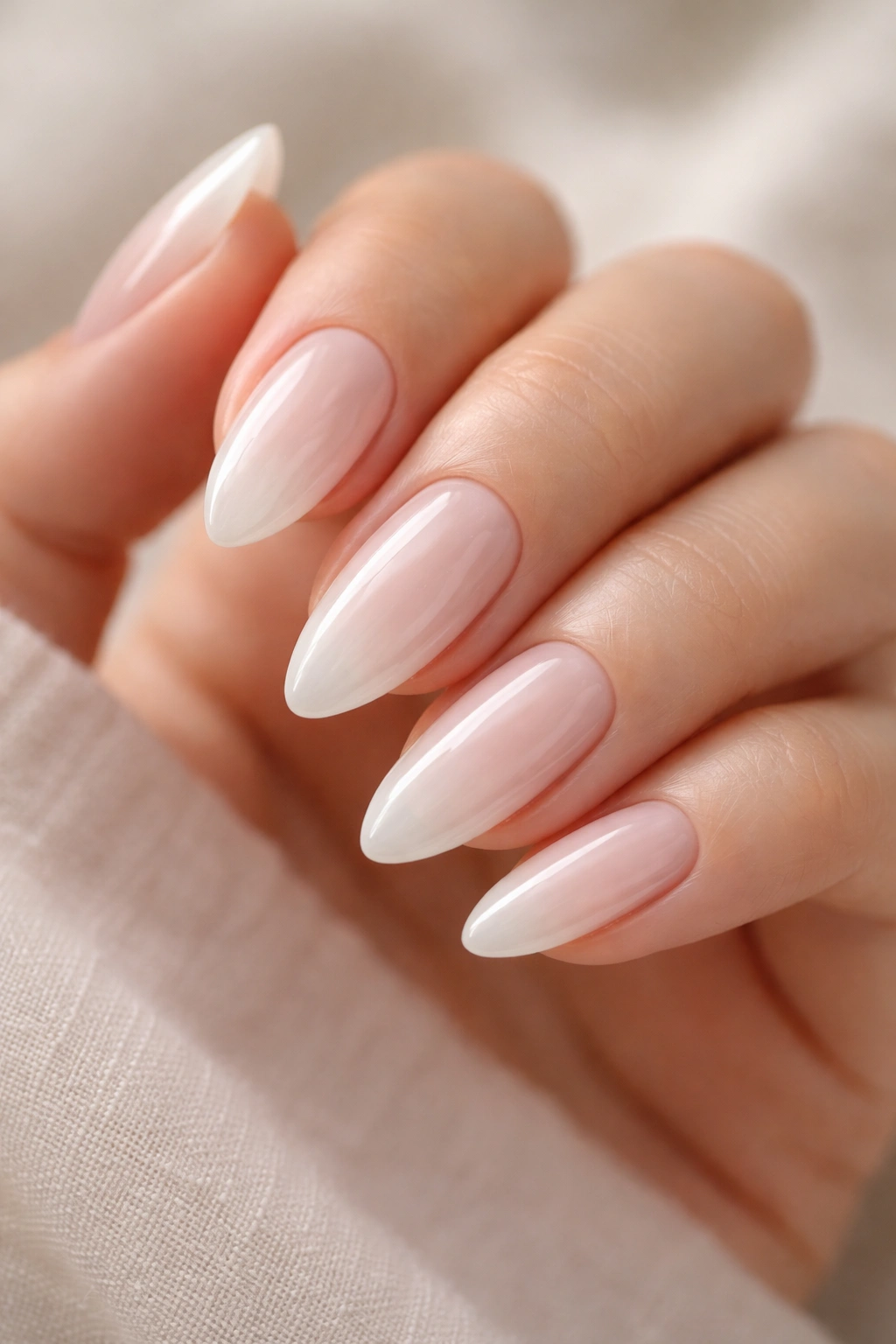 Close-up of soft milky white almond nails with translucent gloss on a neutral backdrop