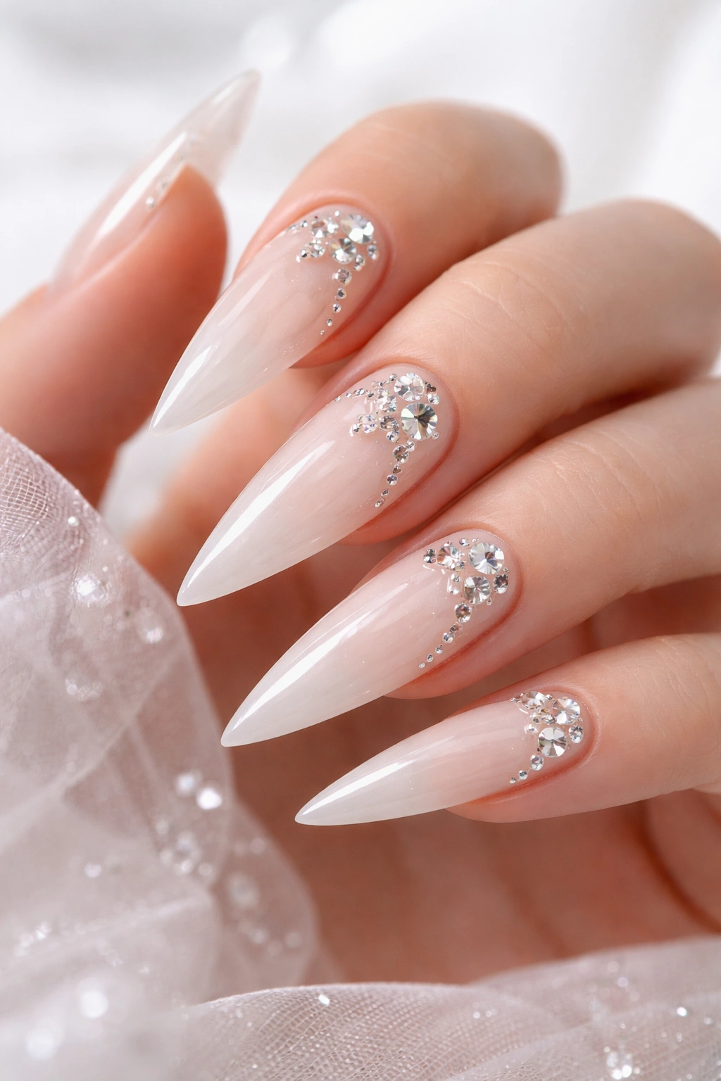 Close-up of clear stiletto nails with milky white base and gem accents