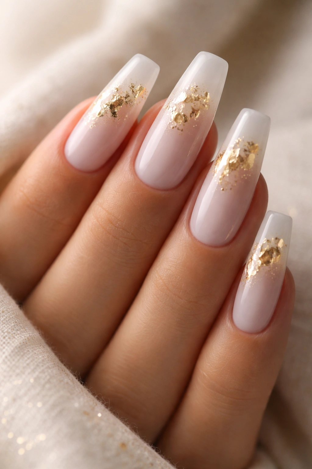 Milky white coffin nails with delicate gold leaf accents on a neutral background