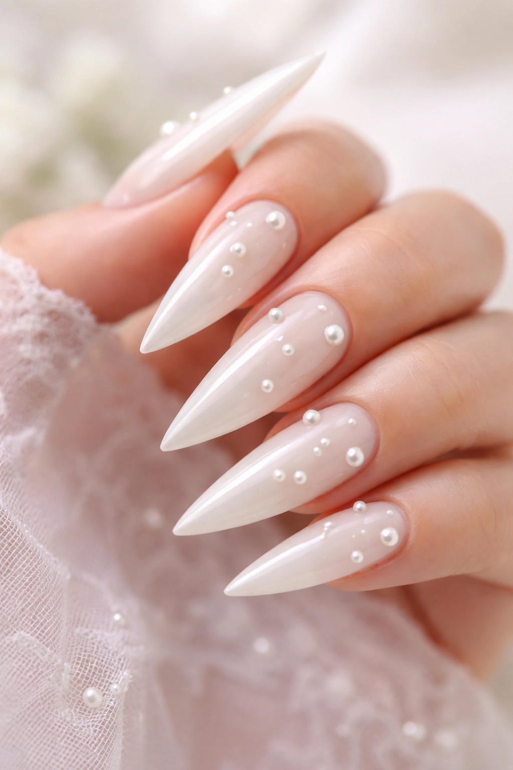 Close-up of a milky white stiletto nail with embedded pearls