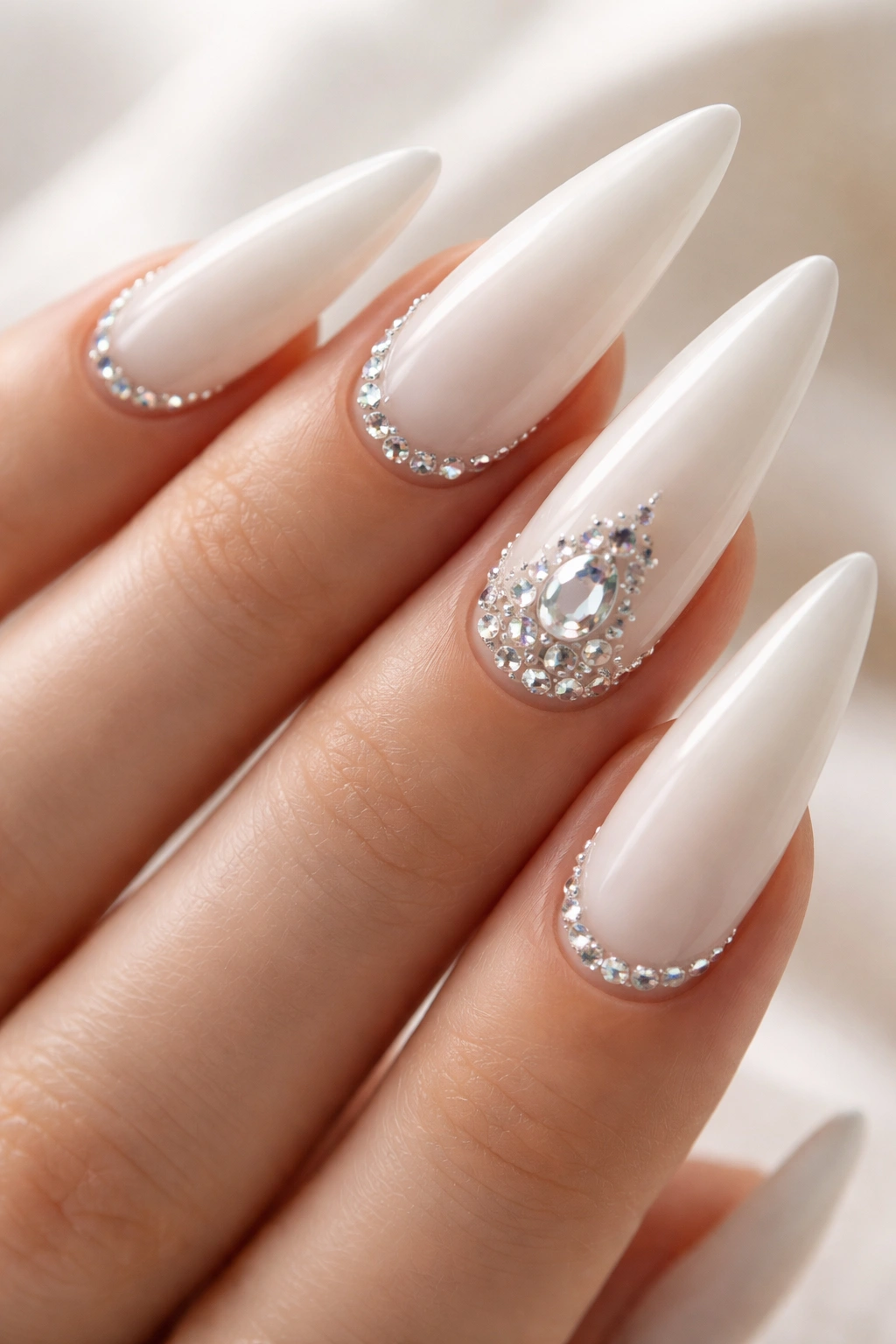 Milky white stiletto nails with delicate rhinestones along the cuticle