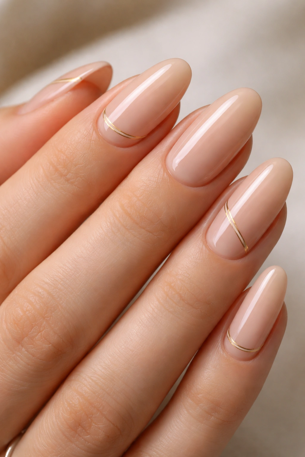 Close-up of long oval nails with a delicate gold line art on nude base