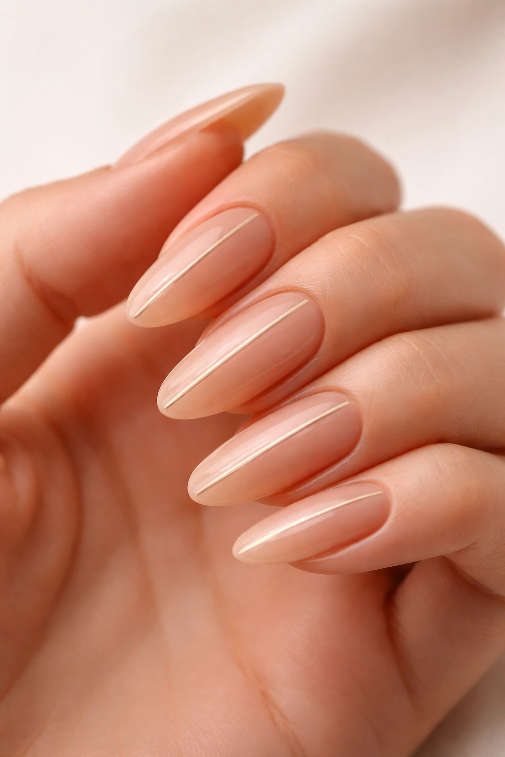Close-up of nude long oval nails with a single thin gold line down the center