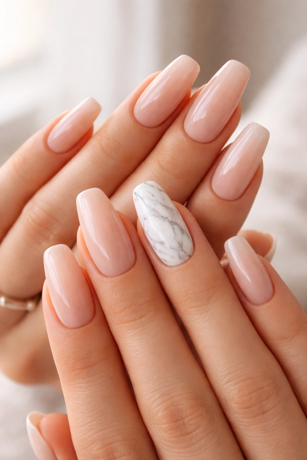 Close-up of nude nails with a single marble-accent nail on the ring finger
