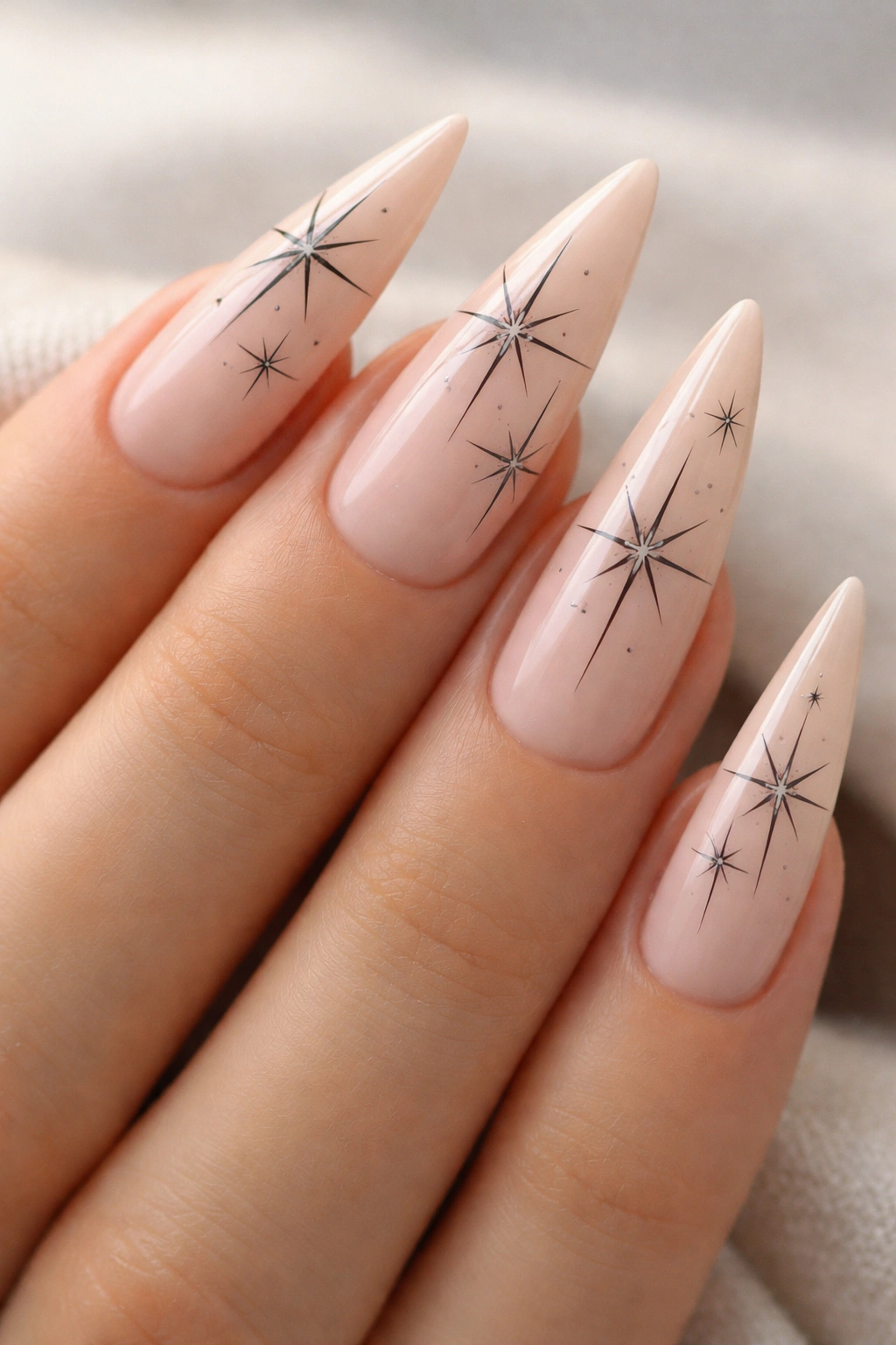 Stiletto nails with minimalist black line-art stars on a nude base