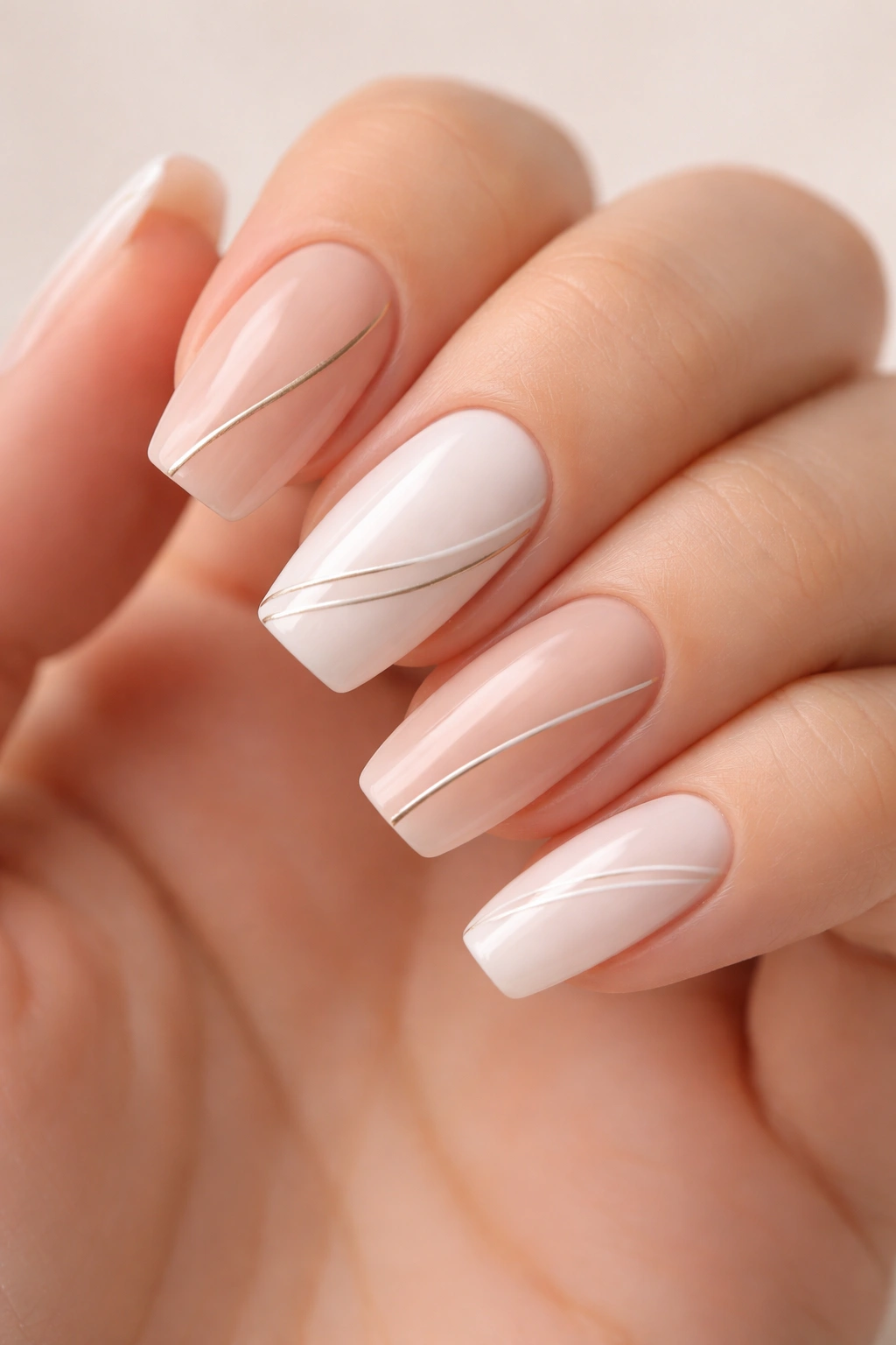 Close-up of medium-length acrylic nails with thin gold lines on nude base