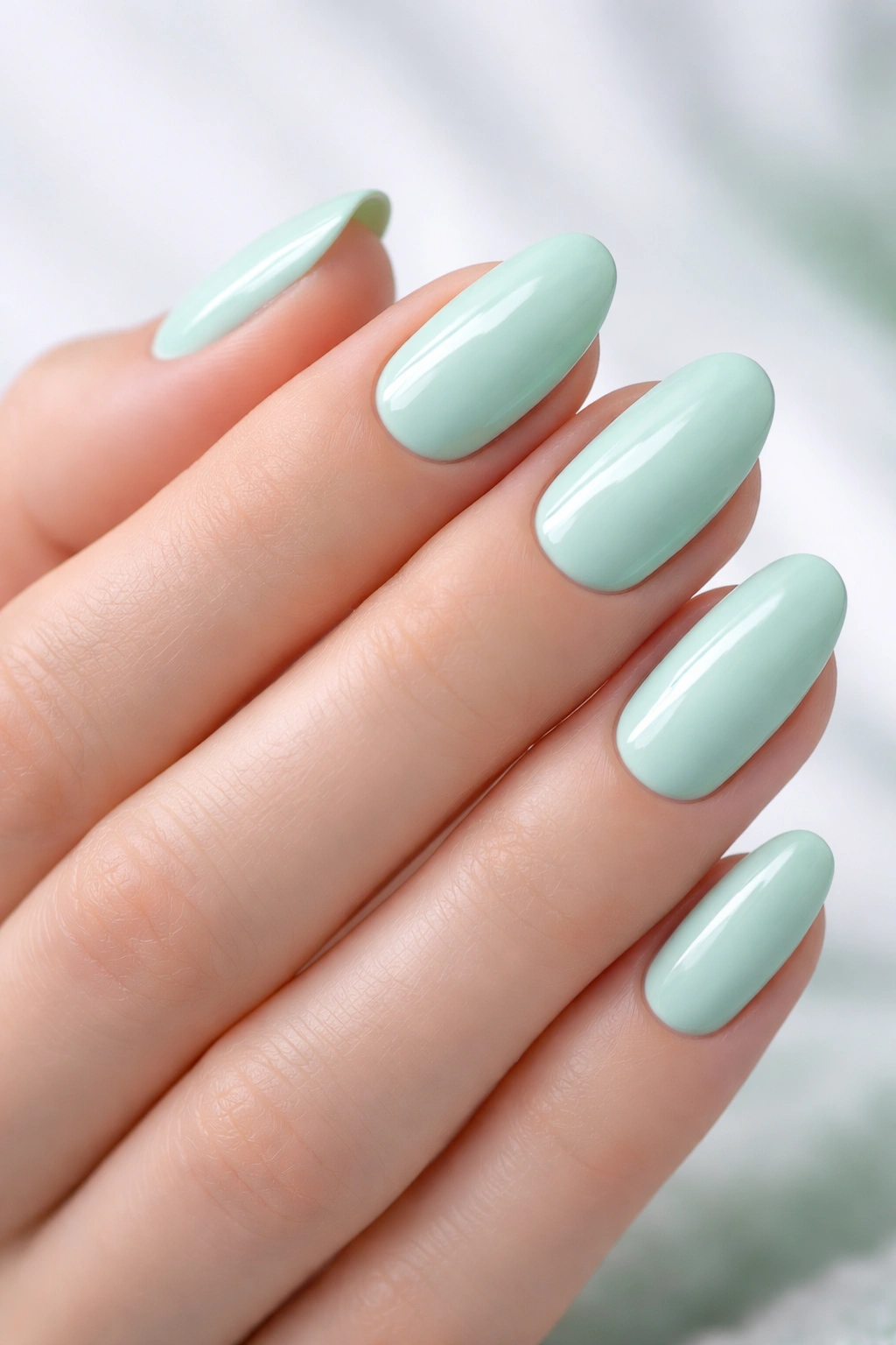 Close-up of a hand with nails painted mint green on a simple backdrop