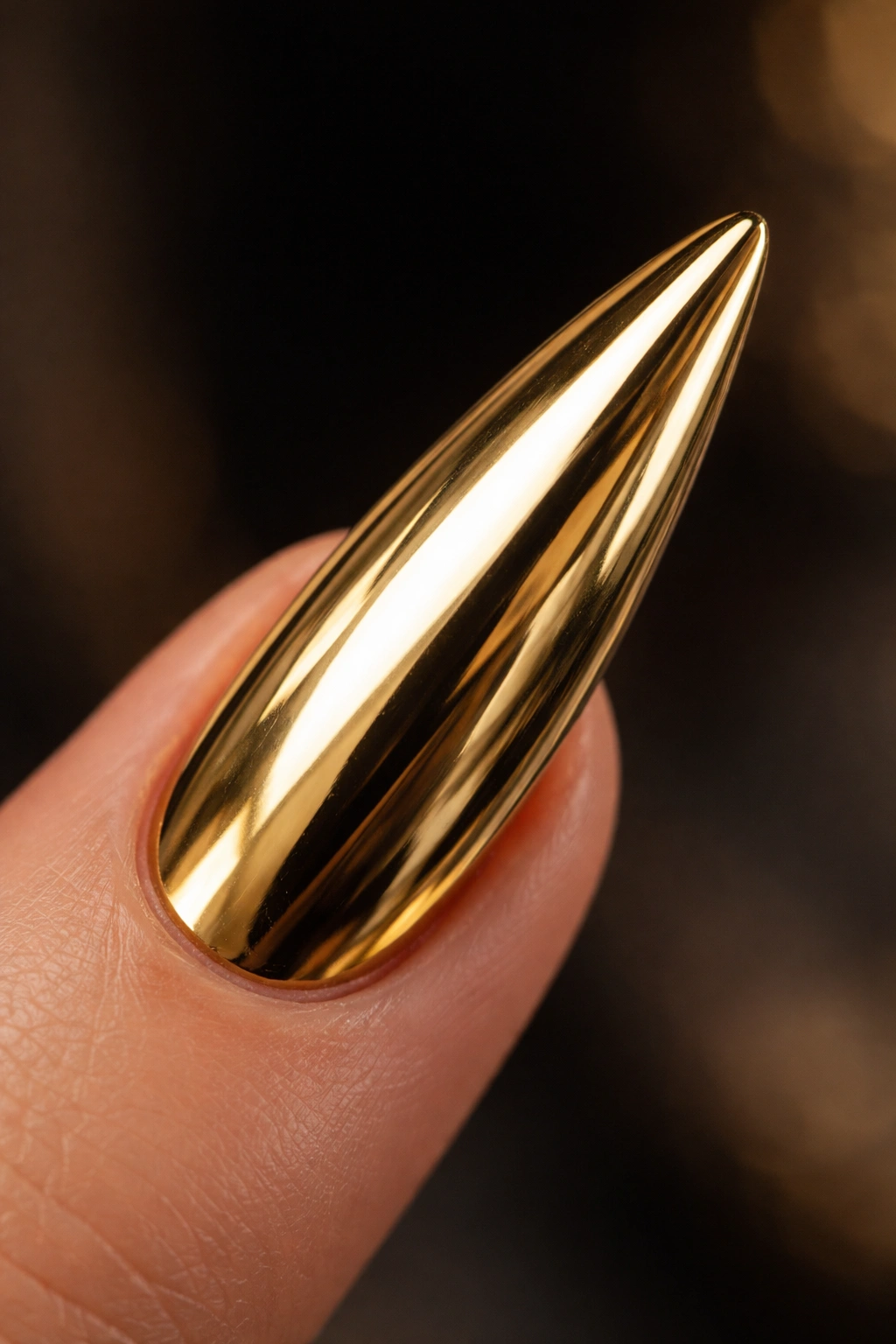 Close-up of a single gold mirror finish stiletto nail with reflective chrome surface