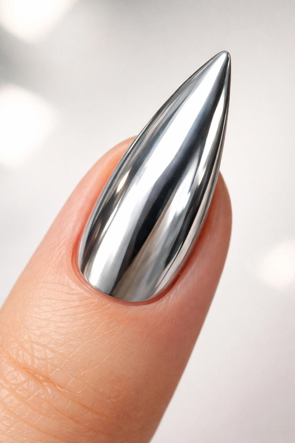 Close-up of a single stiletto nail with a mirror silver high-shine chrome finish