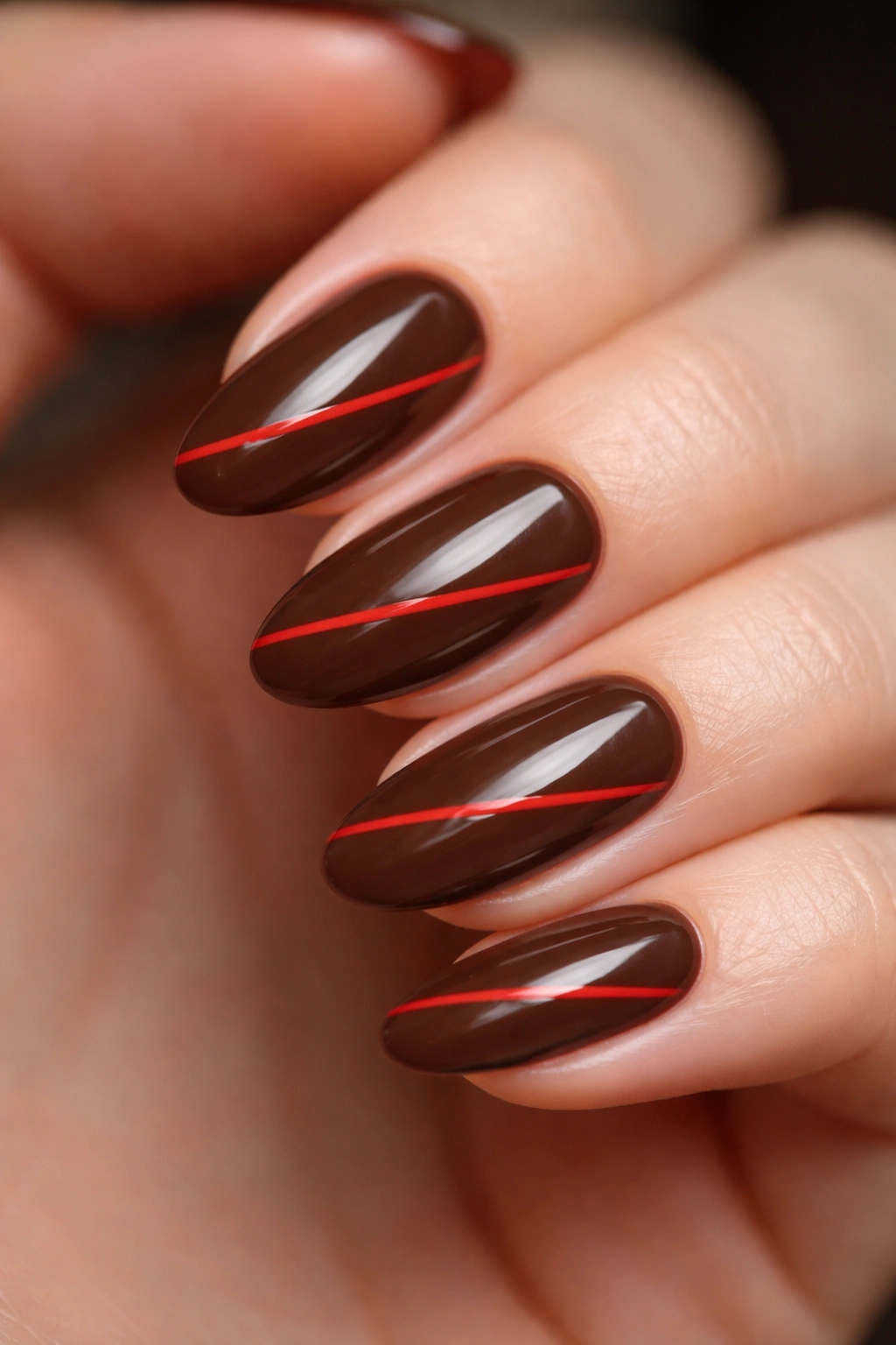 Mocha base nails with red diagonal geometric lines on short almond nails.