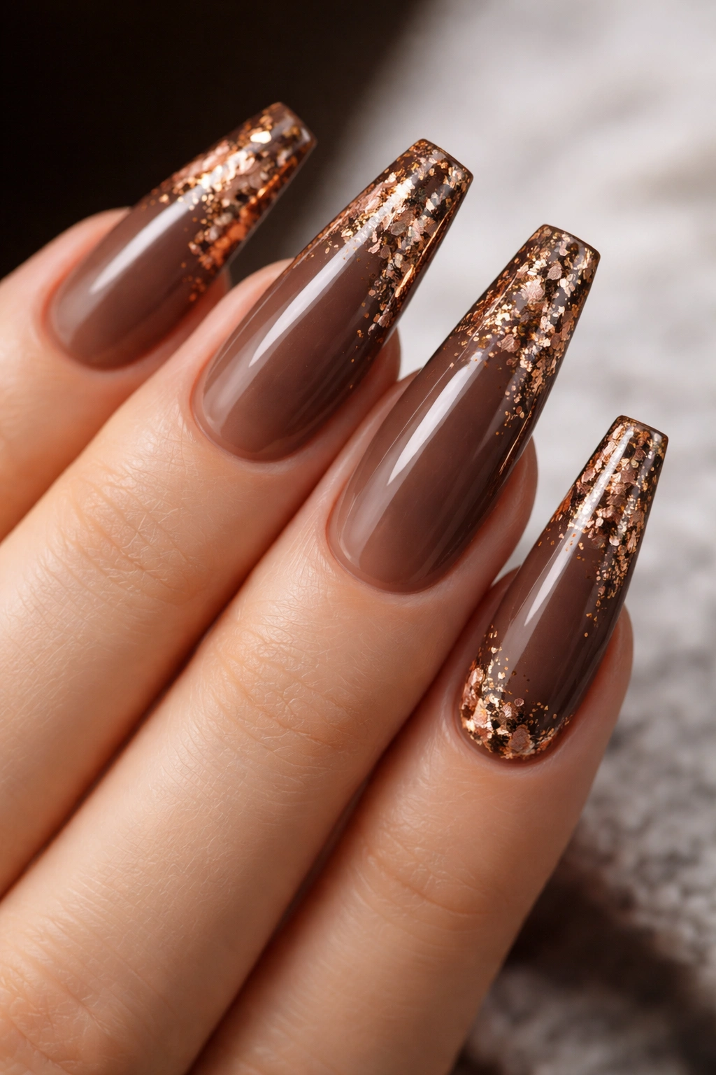 Close-up of mocha brown nails with bronze foil shards