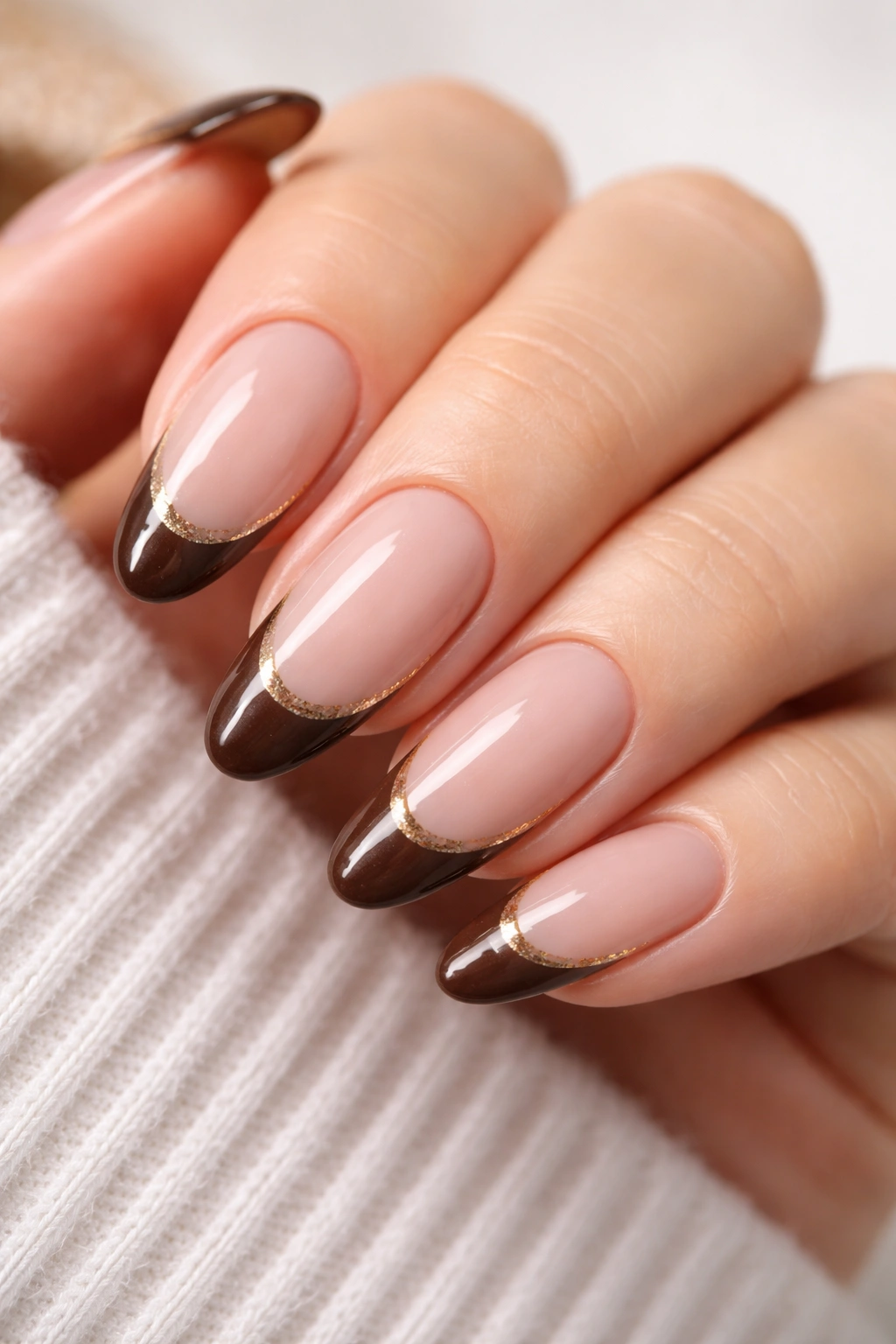 Close-up of almond nails with mocha French tips and a thin gold line