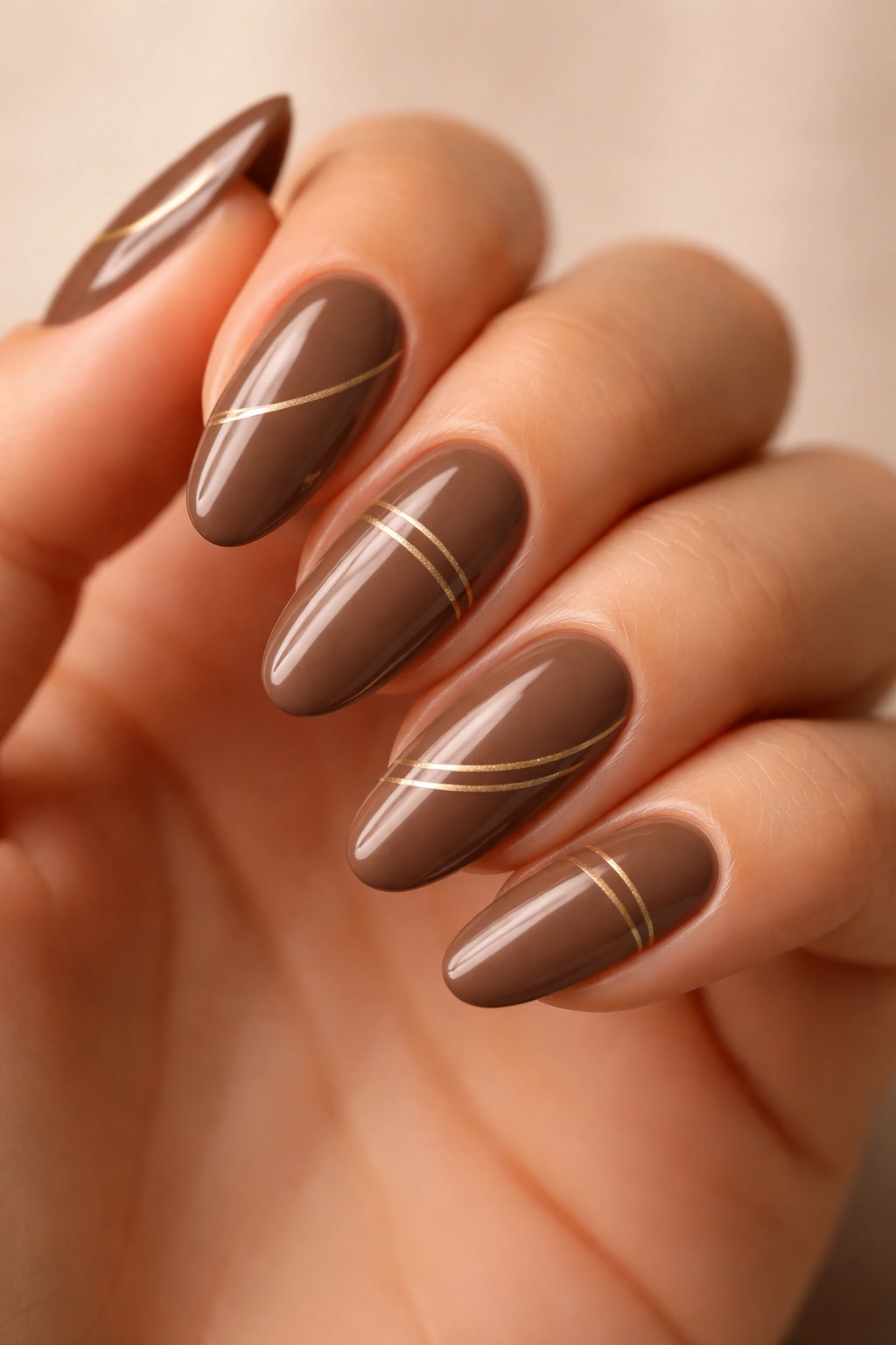 Mocha nails with delicate gold lines on a neutral background