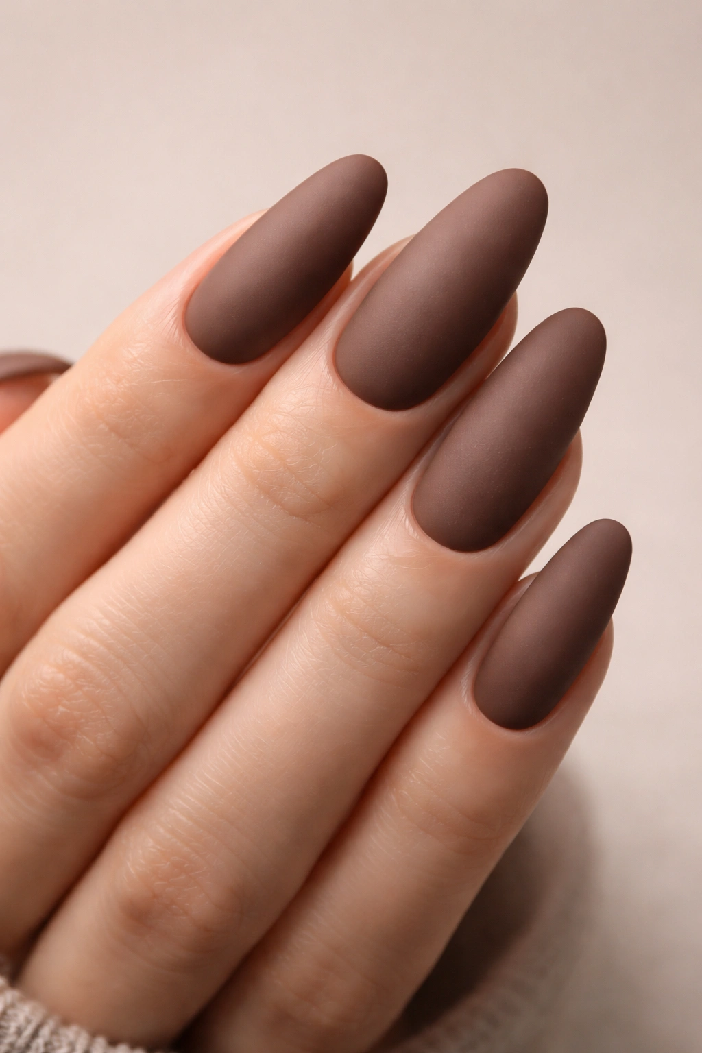 Close-up of long oval nails with a matte mocha finish on a neutral background