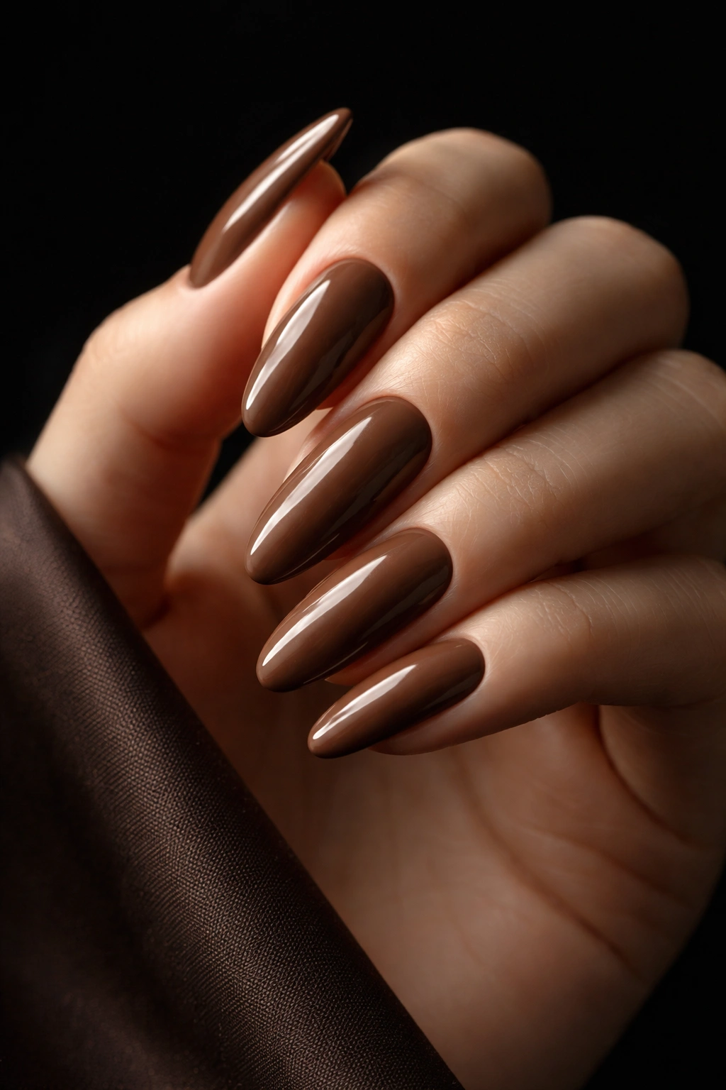 Elegant close-up of long oval mocha nails on dark backdrop