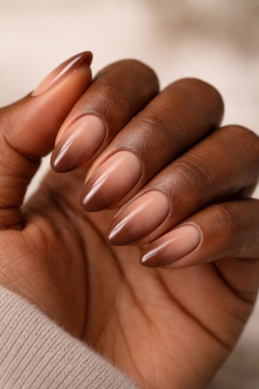Close-up of short almond nails with mocha ombré fade on dark skin