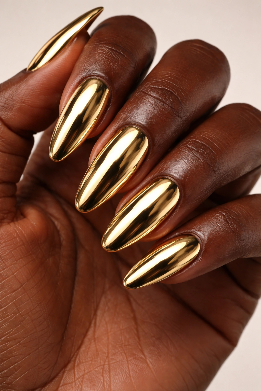 Close-up of dark-skinned hand with molten gold chrome nails reflecting light
